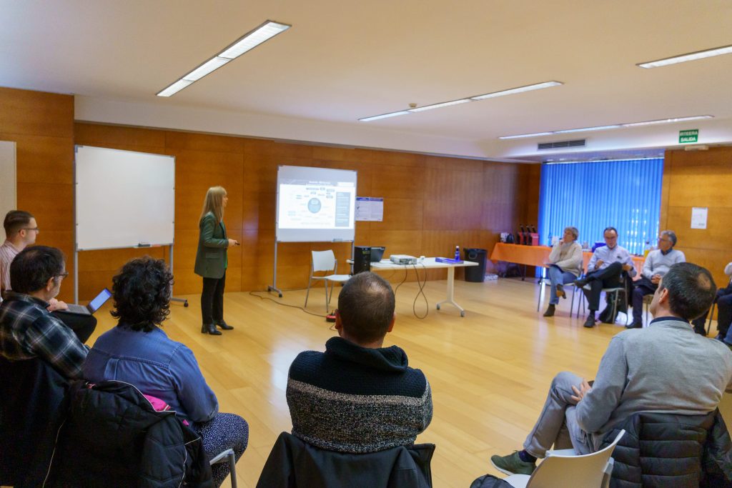 Sesión del grupo motor del Laboratorio Urbano Barakaldo: una ponente presenta ante una pantalla y el resto escucha sentado en círculo